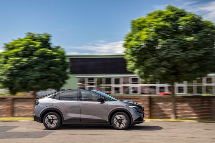 Seitliche Fahraufnahme eines grauen Nissan Leaf vor einer halbhohen Backsteinmauer, hinter der zwei Bäume stehen