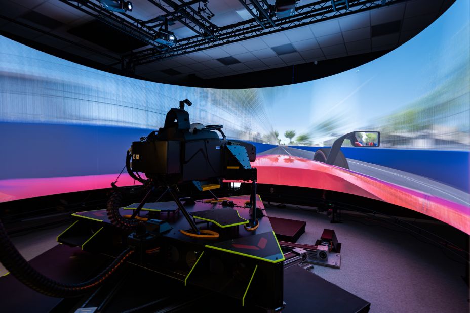 A racecar simulator being operated in a dark room with projections of the race track in front of it.