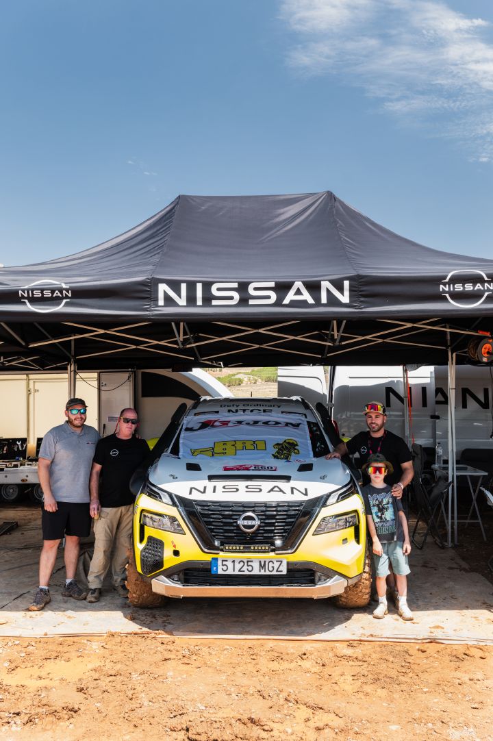 Drei Nissan Teammitglieder und ein Kind stehen neben dem Nissan X‑Trail Rallyeauto