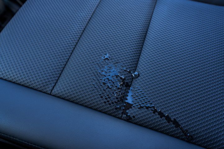 Neuer 2026 Nissan X‑Trail N-Trek mit strukturiertem, wasserdichtem CellCloth®-Bezug und schwarzer Lederverkleidung, auf dessen Oberfläche sich eine klare Flüssigkeit angesammelt hat. Die Flüssigkeit unterstreicht die wasserabweisenden Eigenschaften des Sitzes und den Kontrast zwischen Stoffstruktur und Leder.