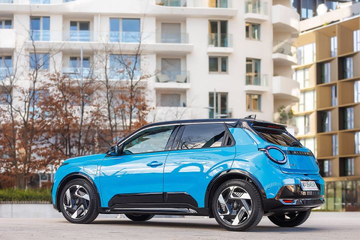 Blick von schräg hinten auf einen leuchtend blauen Nissan Micra mit schwarzem Kontrastdach, das Fahrzeug parkt vor modernen Wohngebäuden
