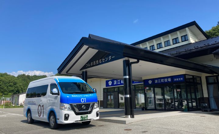 Van da Nissan branca com detalhes em azul estacionada em frente a um prédio com letras em japonês