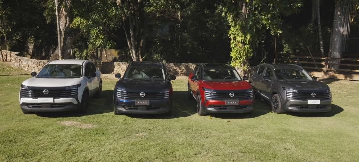 Cuatro unidades Nissan Kicks de diferentes colores estacionadas sobre una zona de césped, vistas de frente y alineadas en un entorno al aire libre rodeado de árboles y vegetación.